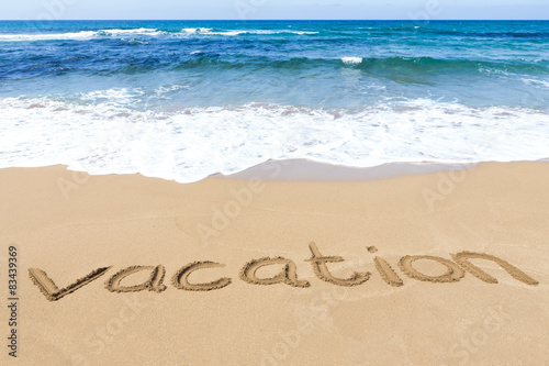 word vacation written on sandy beach at sea