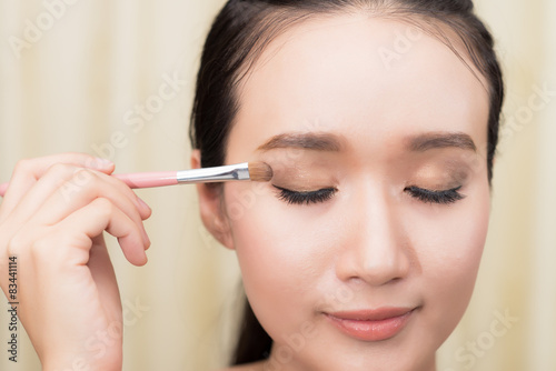 Portrait of pretty young woman applying cosmetic paint brush mod