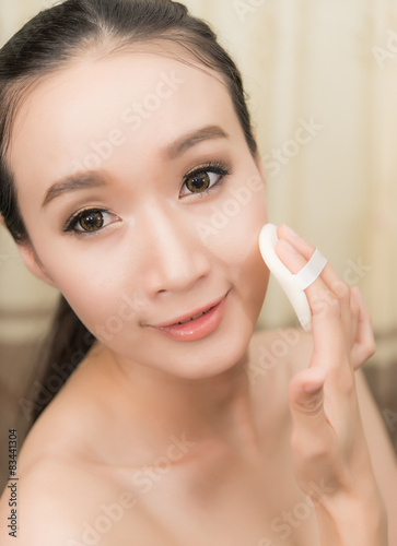 Young Woman applying foundation on face with Powder puff,model i