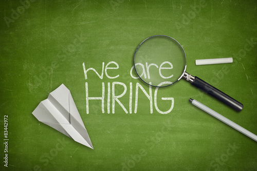 We are hiring concept on green blackboard with magnifying glass