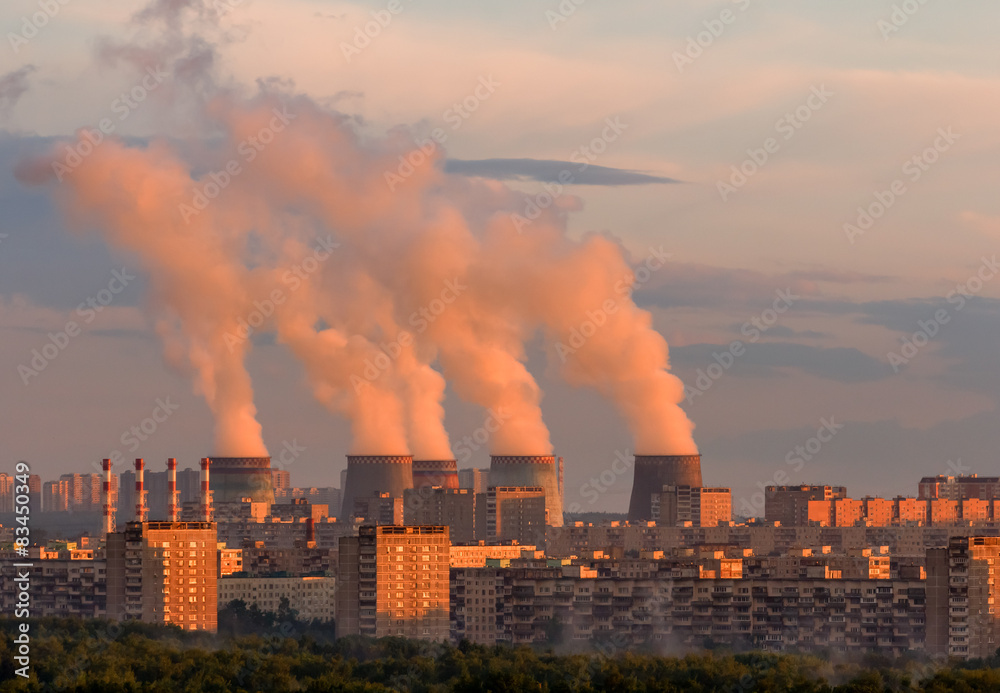 Cooling tower power plant with steam on a background of the city at sunset