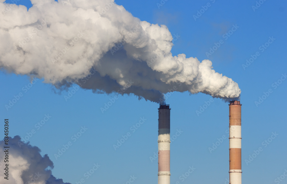 Pipes of thermal power plant with white smoke against the blue sky