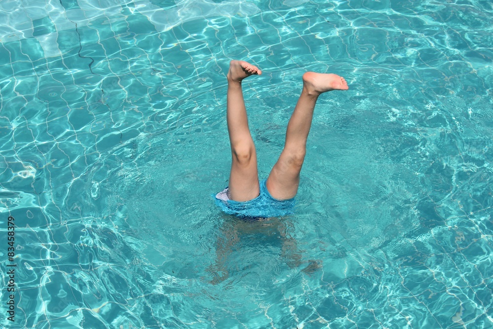 young boy sticks his legs out from the water of pool