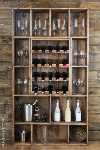 Shelving with wine bottles and glasses on wooden wall background