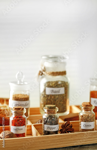 Assortment of spices in glass bottles in box, on light background