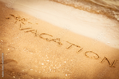 The word vacation written in the sand on a beach