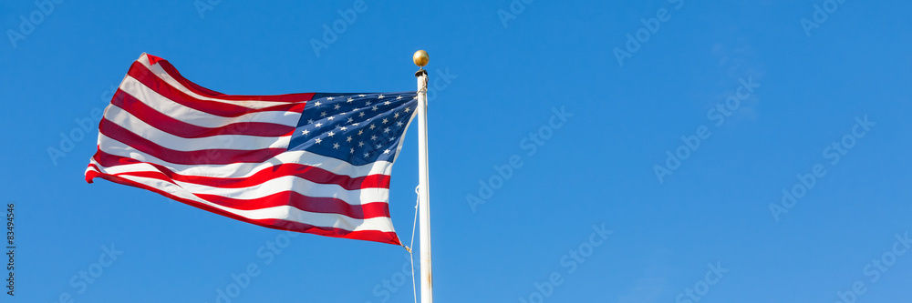Fototapeta premium American flag waving in the wind on blue sky, US flag motion close-up, red white blue flag outdoors in sunlight. United States of America national flag. USA stars and stripes