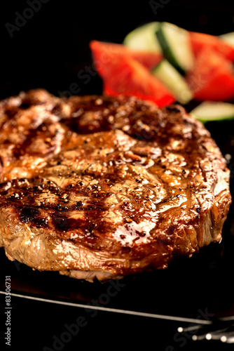 Grilled steak and vegetables on black plate vertical