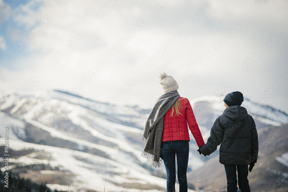 A brother and sister standing side by side in the snow, back view. A brother and sister standing side by side in the snow, back view.