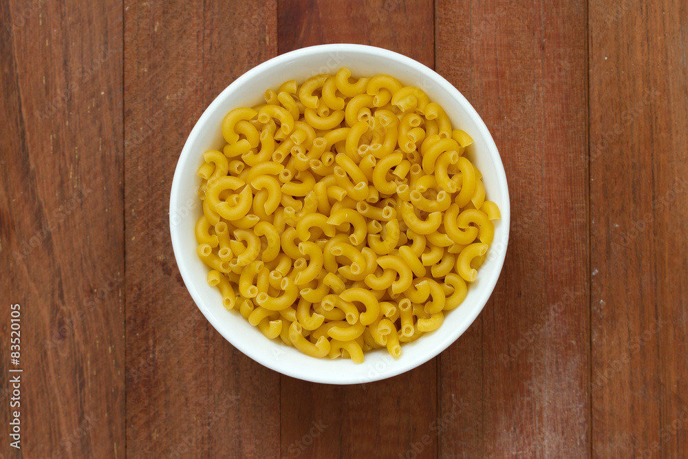 dry pasta in white bowl on brown wooden background dry pasta in white bowl on brown wooden background