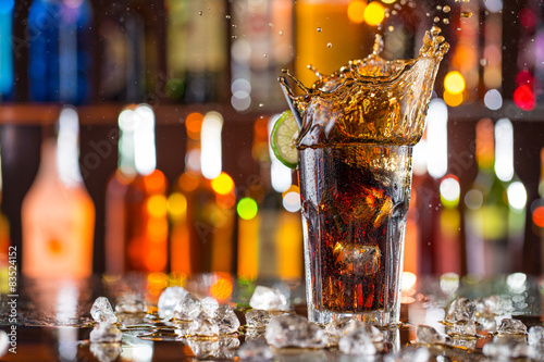 Glass of cola on bar desk with splashing liquid