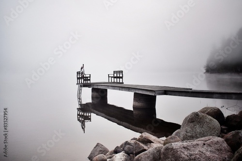 Sweden, Dalarna, Pier reflecting in surface of water in misty, foggy morning