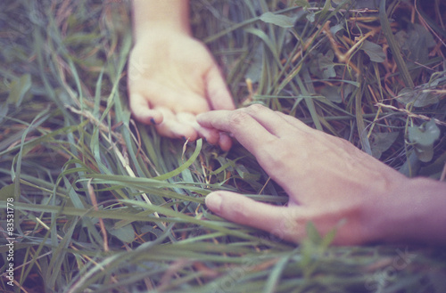 Cropped view of couple's hands on grass, reaching towards each other photo