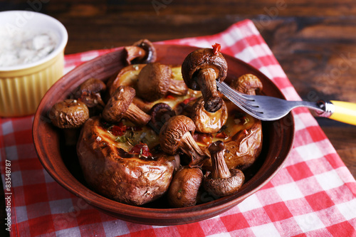 Baked potatoes with mushrooms in bowl and sauce on table close up