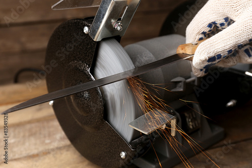 Tableau sur toile Knife sharpener and hand with blade on wooden table, closeup