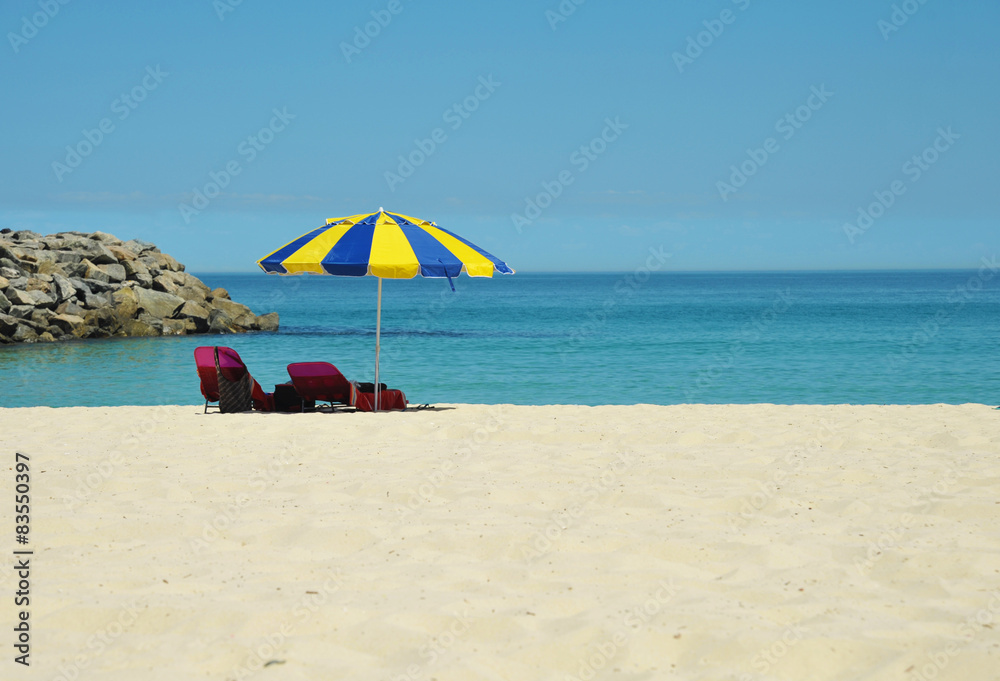 Sun lounger under an a blue-yellow umbrella on an empty beach