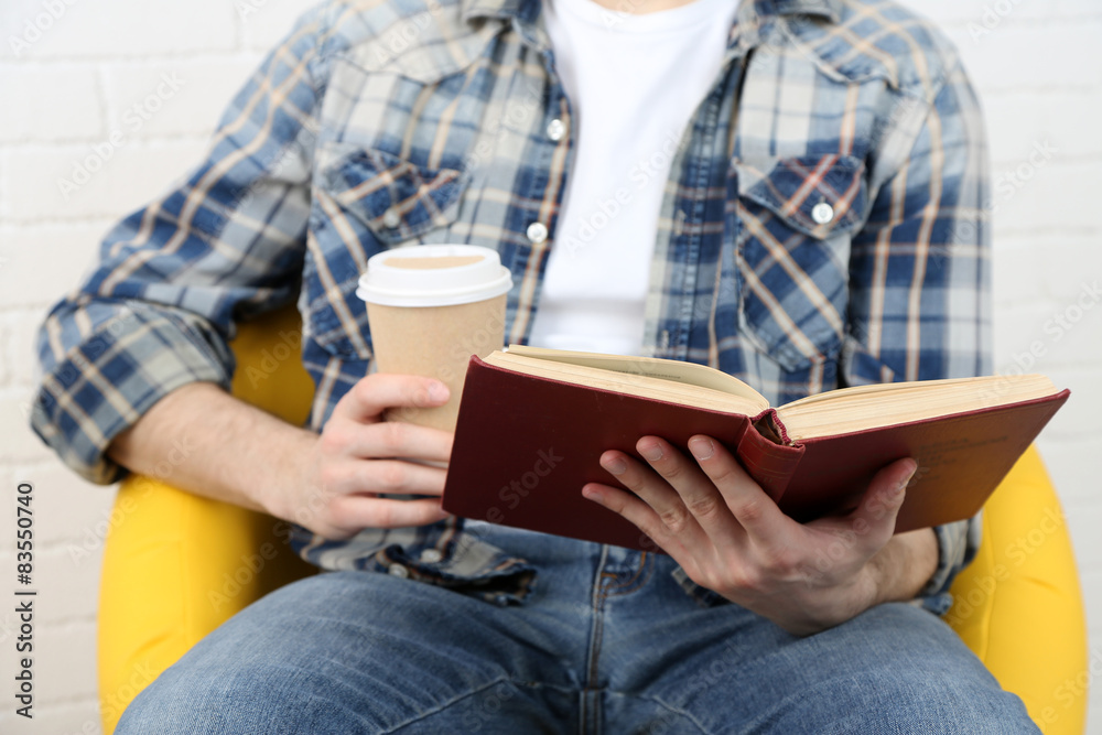 Fototapeta premium Young man reading book, close-up, on light background