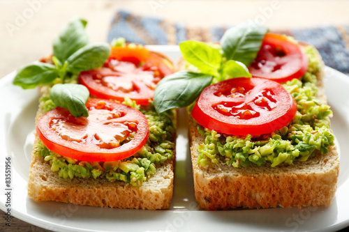 Vegan sandwich with avocado and vegetables on plate, on wooden background