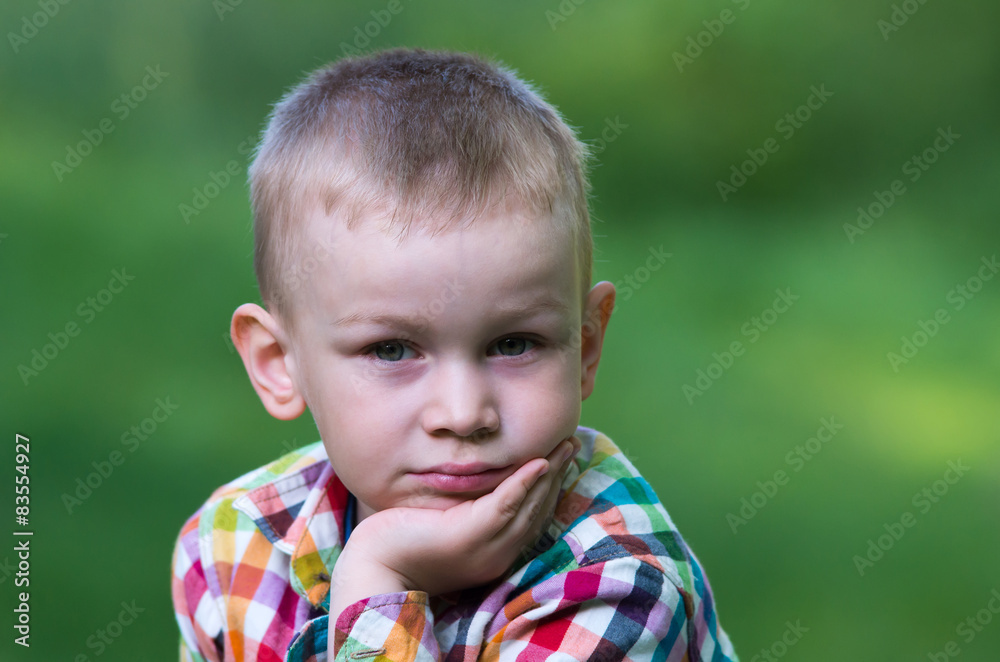 A little boy sitting on the grass and looking thoughtfully ahead A little boy sitting on the grass and looking thoughtfully ahead