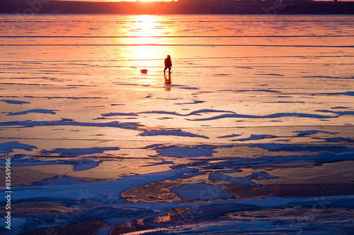 The lonely figure of a man walking on the frozen river at sunset, the reflection of the sun created the effect of fire of the desert.