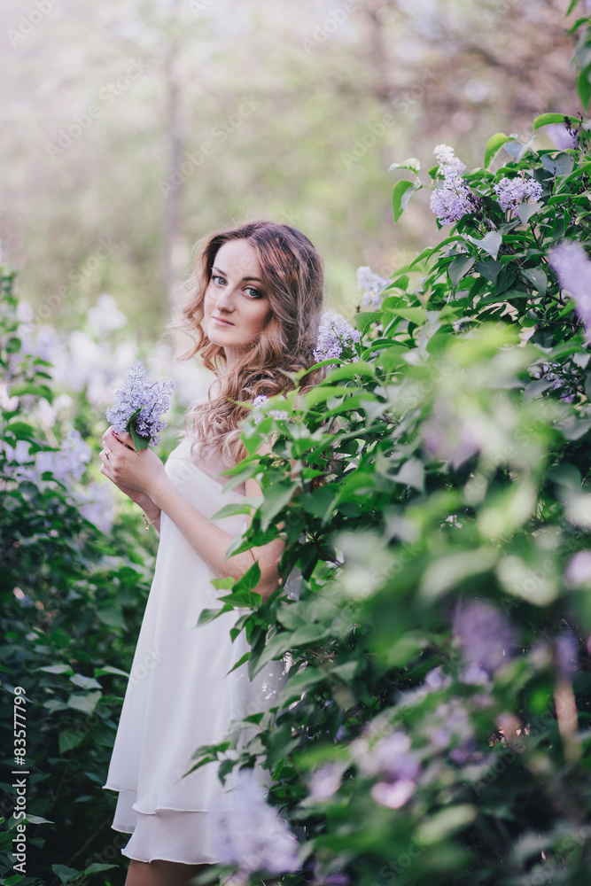 Beautiful young woman with long curly hair posing with lilacs Beautiful young woman with long curly hair posing with lilacs
