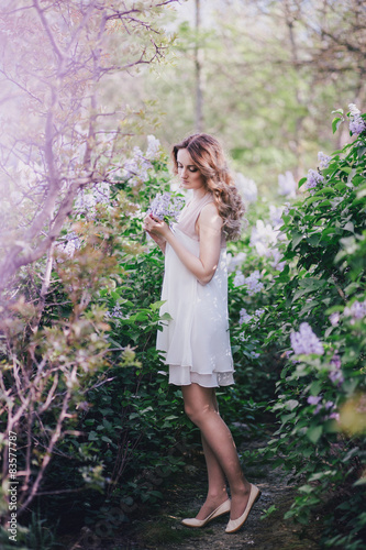 Beautiful young woman with long curly hair posing with lilacs