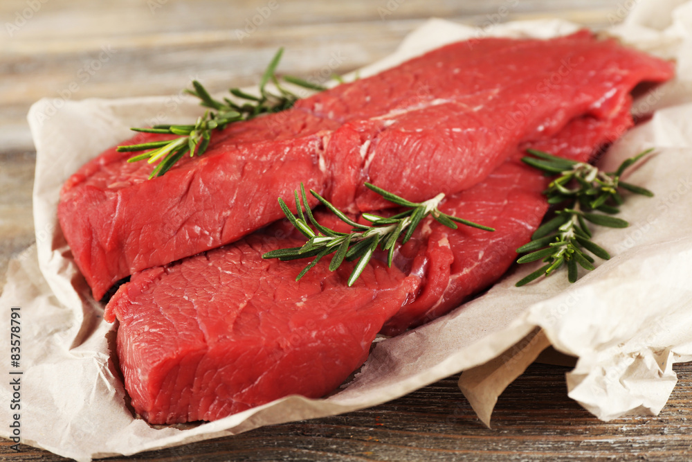 Raw beef steak with rosemary on paper on wooden background