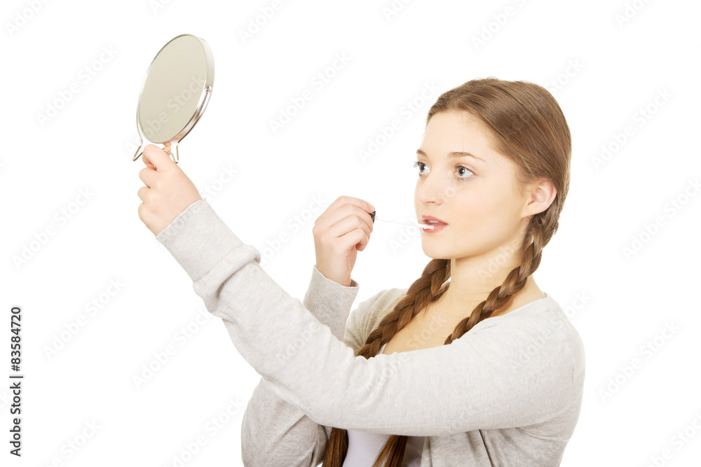 Teen woman applying lipstick looking at mirror. Teen woman applying lipstick looking at mirror.