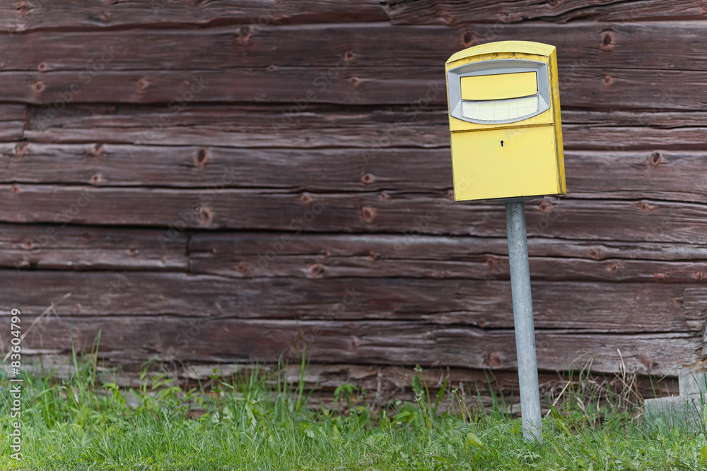 Traditional yellow postbox in front og a wooden wall Traditional yellow postbox in front og a wooden wall