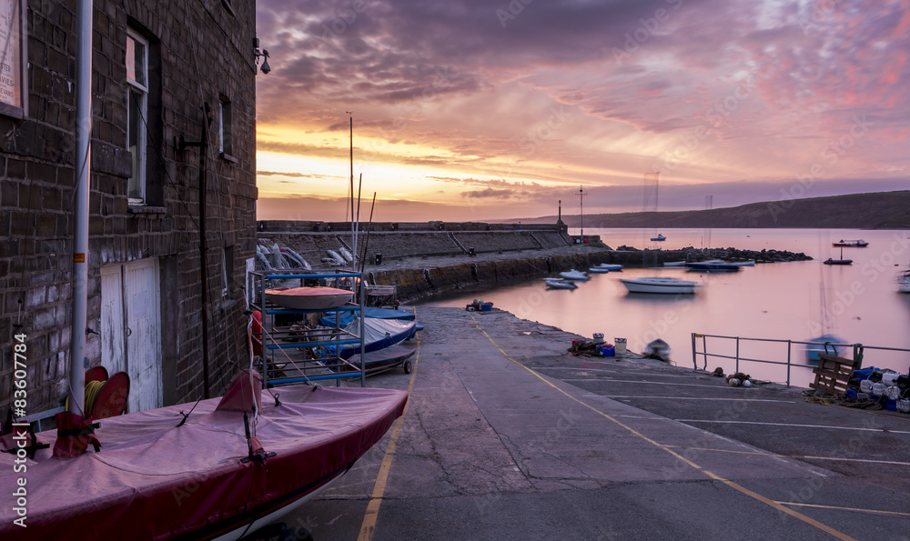 Naklejka premium Dawn breaking over a road leading to a stone harbour wall in New Quay, Wales