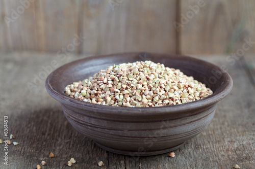 Dry green buckwheat in a clay bowl on wooden table