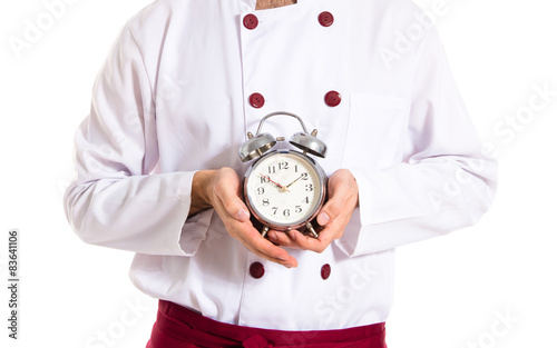 Surprised chef holding a clock over white background