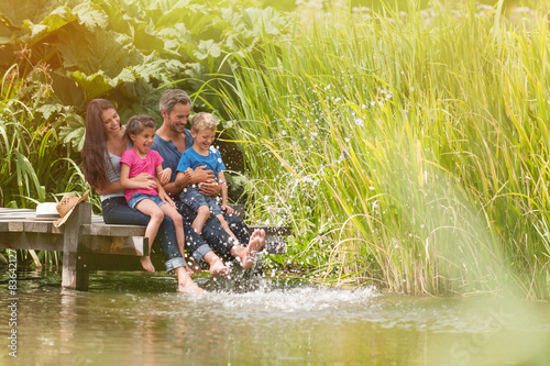 Fotografi happy family sitting at the edge of a pontoon, feet in the river