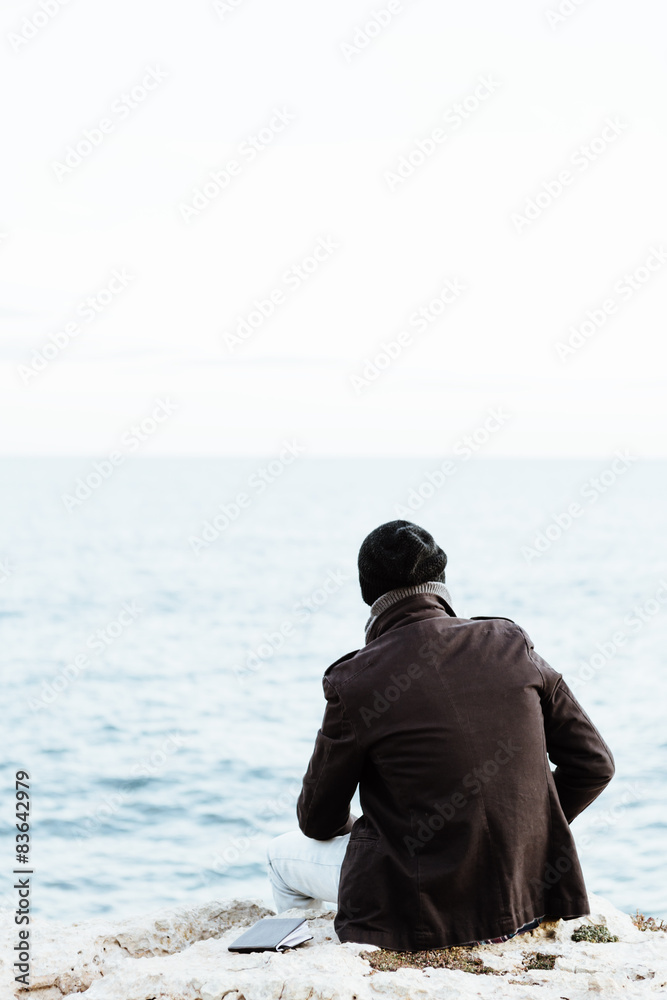 Man watching the ocean from a cliff, back view.