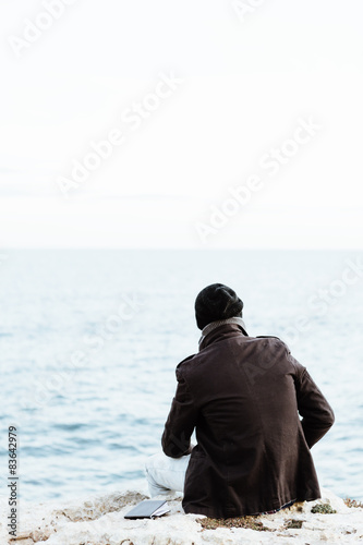 Man watching the ocean from a cliff, back view.