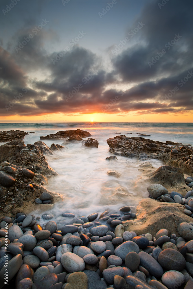 Early morning landscape of ocean over rocky shore and glowing su
