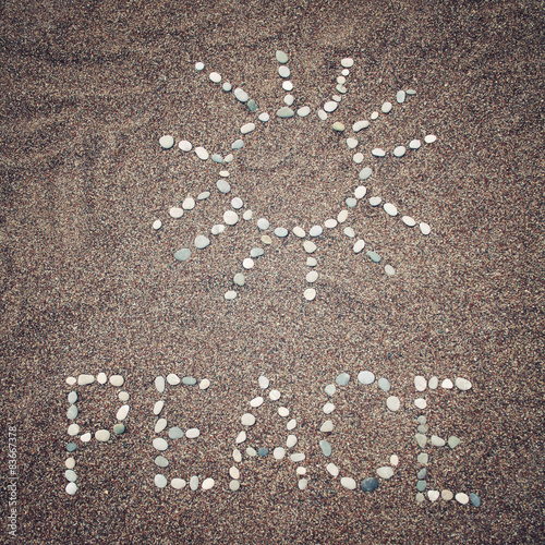 Peace word and sun symbol on the sand - toned photo.
