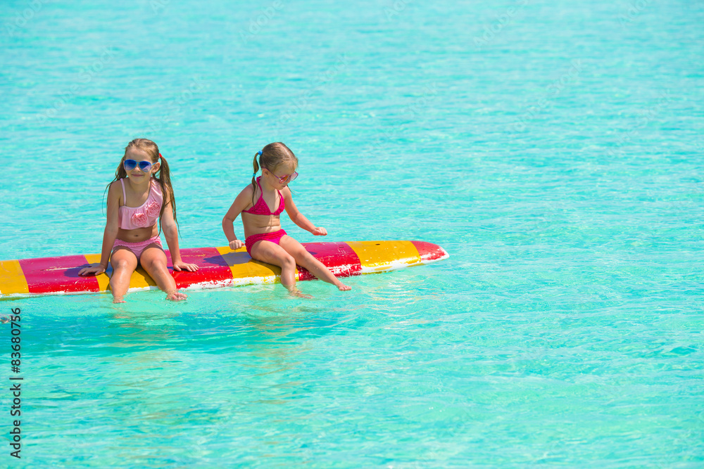 Little adorable girls on a surfboard in the turquoise sea