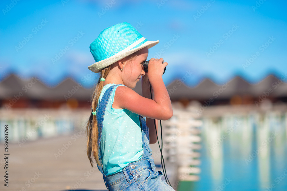 Little girl looking through binoculars in sunny day during