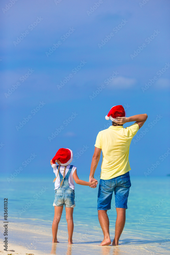 Little girl and happy dad in Santa Hat during beach vacation Little girl and happy dad in Santa Hat during beach vacation