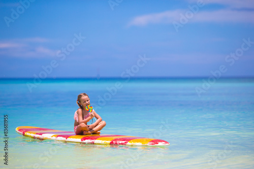 Little girl with lollipop have fun on surfboard in the sea © travnikovstudio