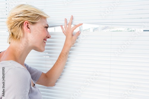 Slika na platnu Curious blonde woman looking through venetian blind