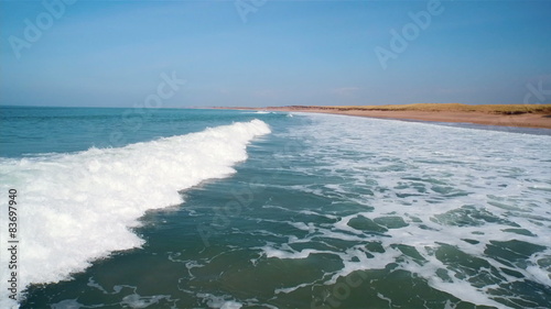 Beautiful drone footage of ocean waves against clear sky. Tracking shot of tidal waves reaching beach. As the waves crash at shore they create a texture from sea foam. HD 1080 video.
