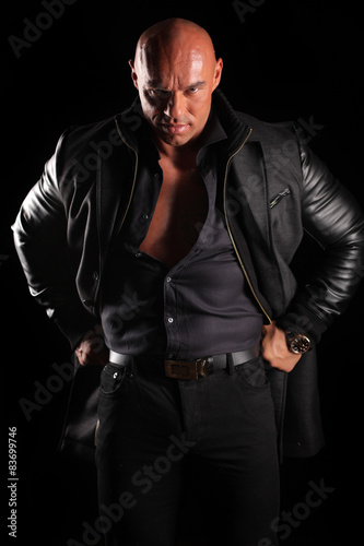 muscular bald man posing in a jacket on a black background