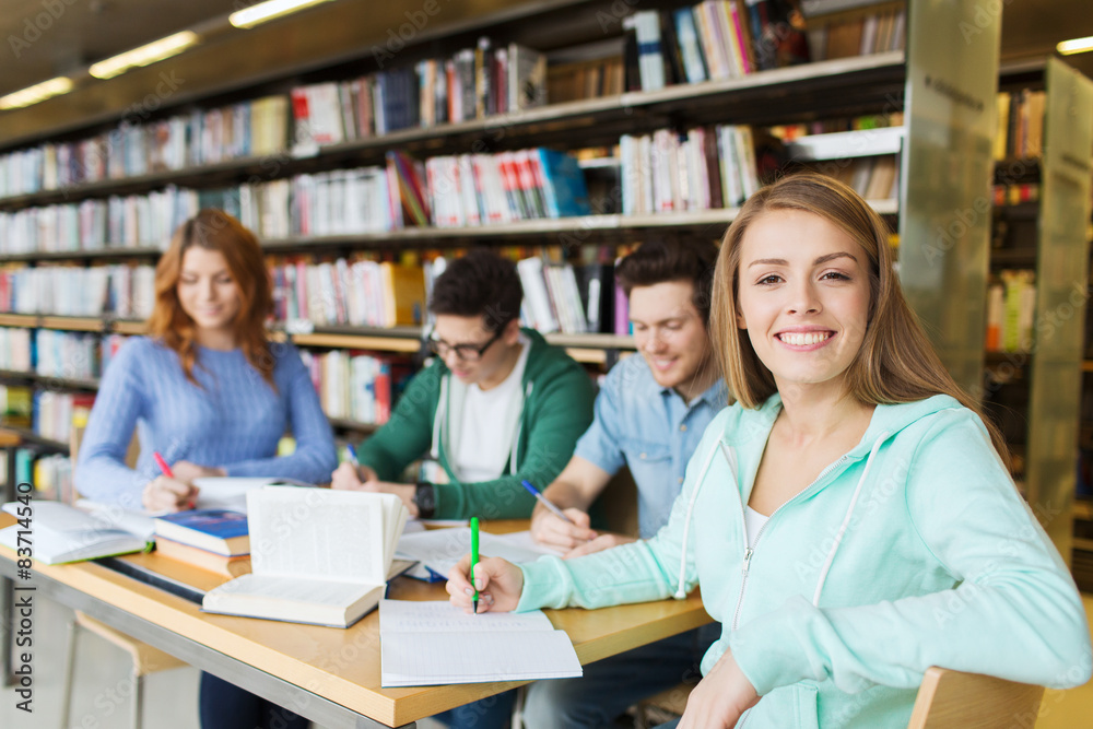 happy student girl writing to notebook in library