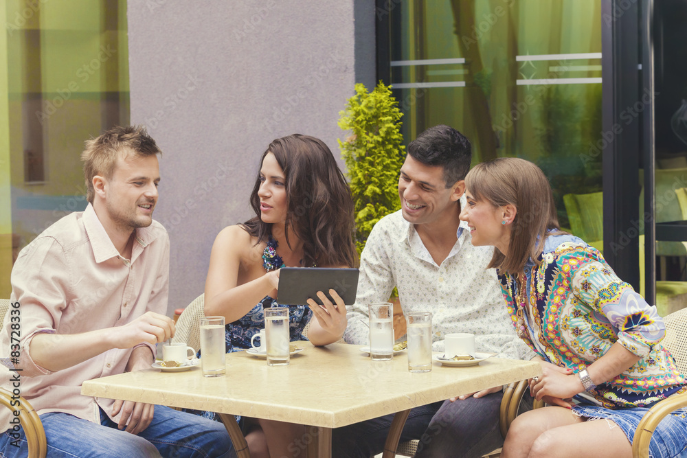Fototapeta premium Friends looking at pictures on tablet in cafe