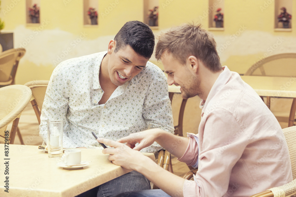 Two men sitting at cafe looking at tablet and smiling Two men sitting at cafe looking at tablet and smiling