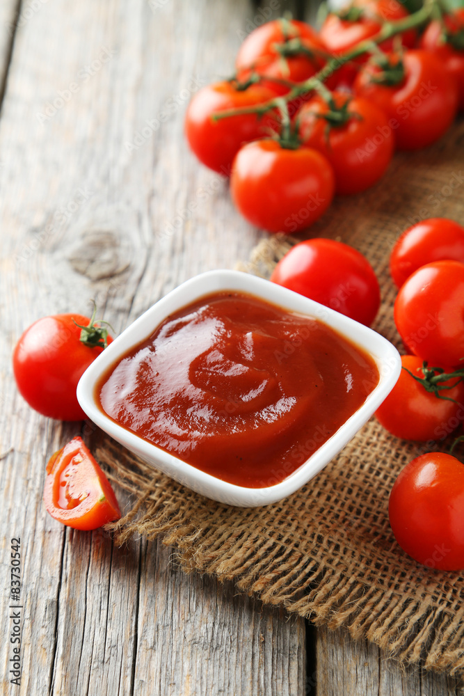 Fresh tomatoes with bowl of ketchup on wooden background Fresh tomatoes with bowl of ketchup on wooden background