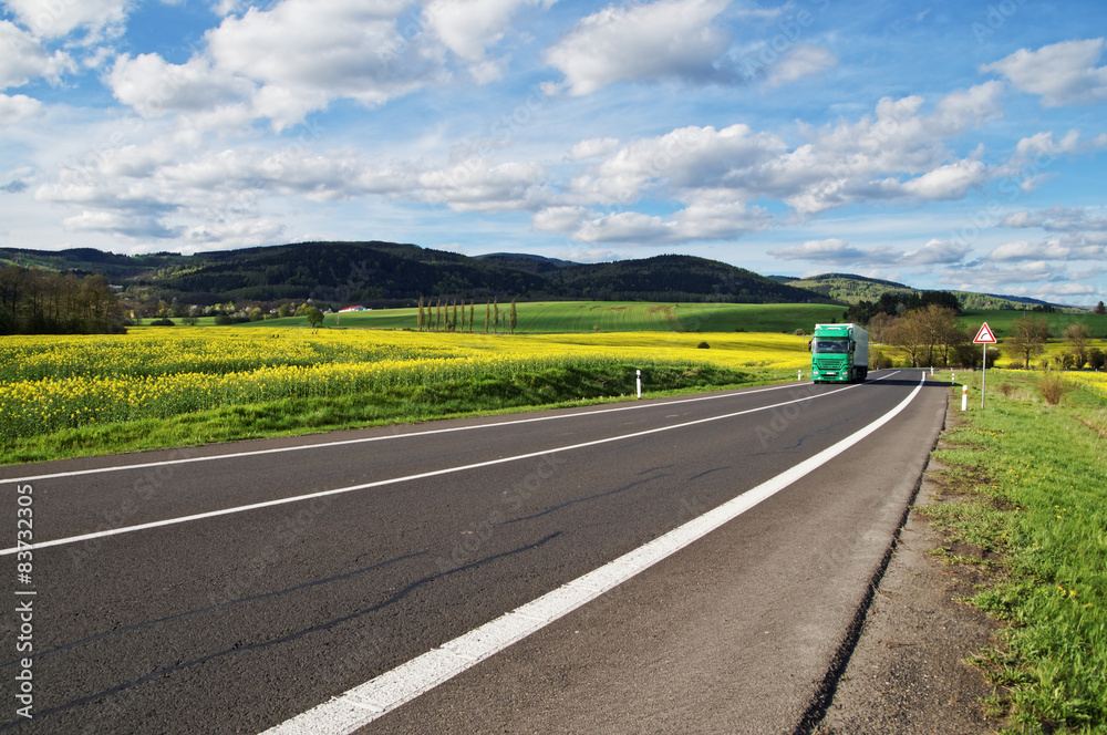 Green truck arrives on road between the rapeseed field Green truck arrives on road between the rapeseed field