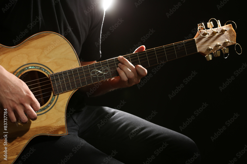 Fototapeta premium Young man playing on acoustic guitar on dark background